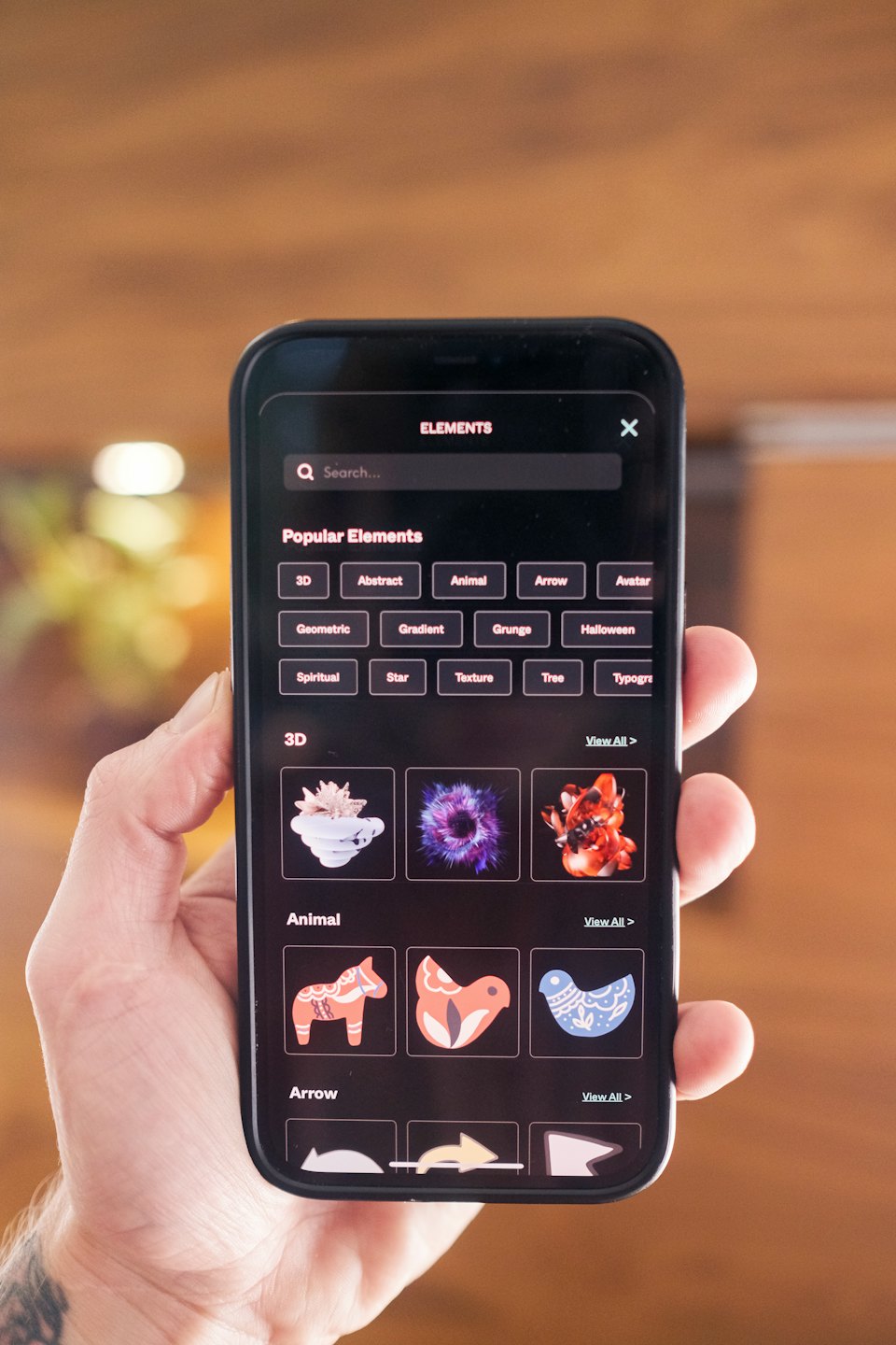 A hand holding a smartphone displaying a design element app.
